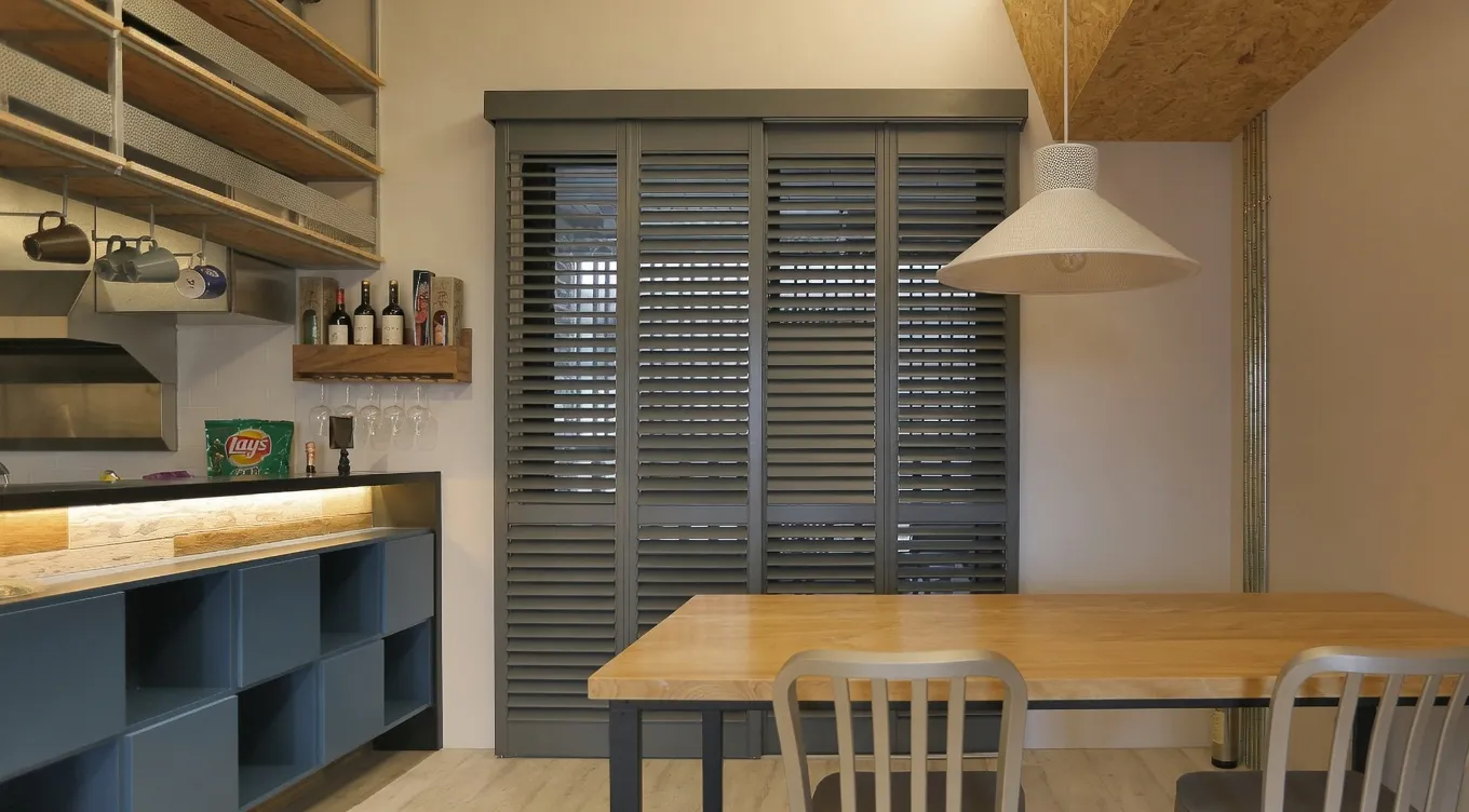 Dark track-mounted shutter panels covering a sliding glass door in a dining area