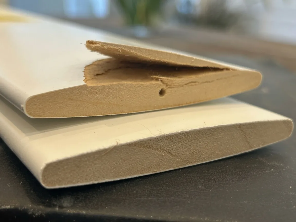A broken MDF shutter louver split open at the end, showing the composite core, next to an intact louver