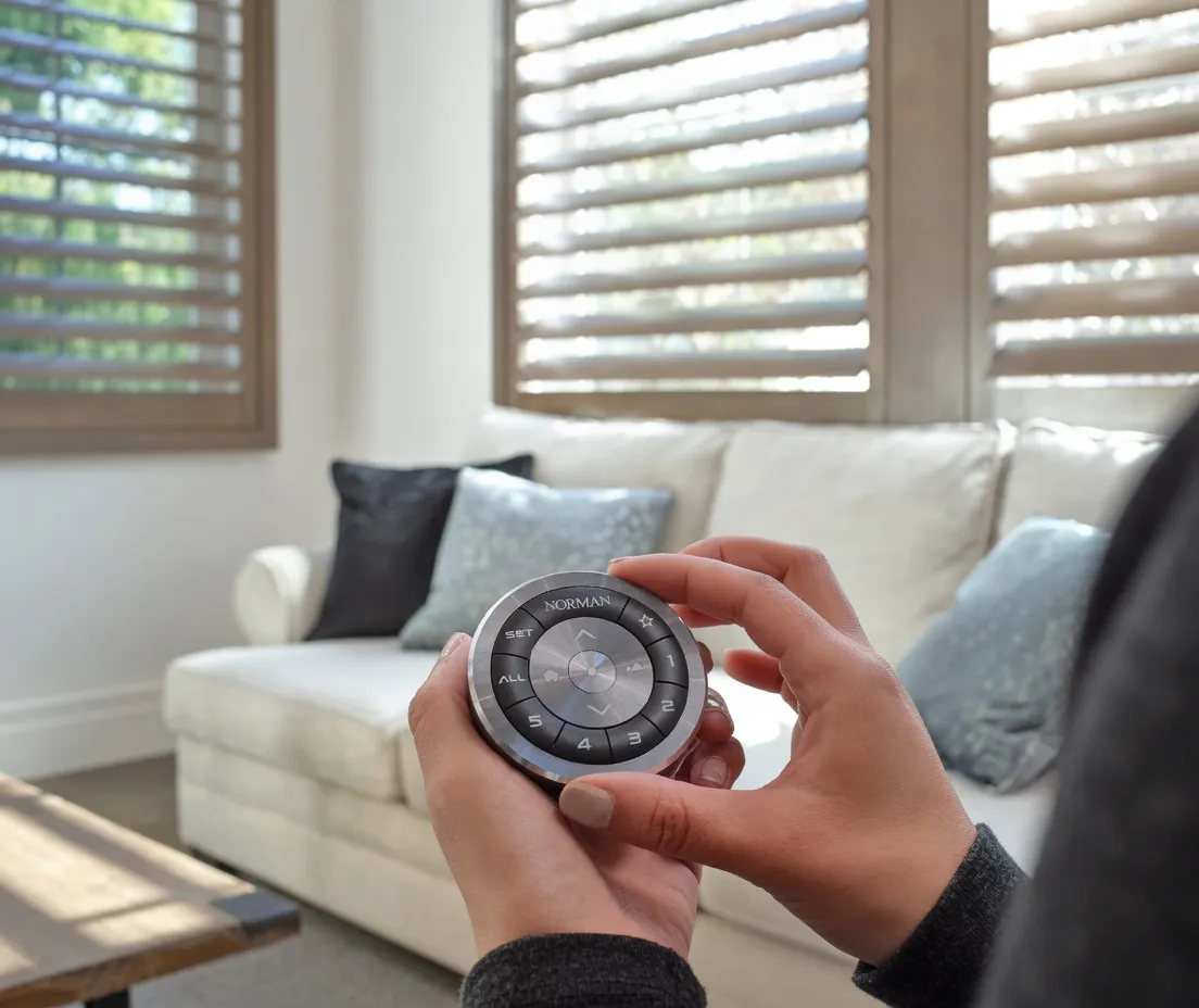 A hand-held Norman remote for motorized shutter louver tilt, with shutters in the background